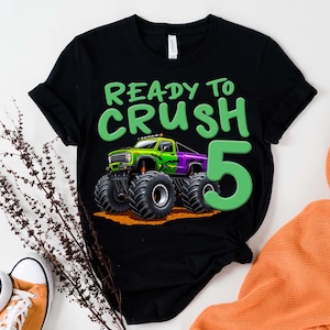 May include: Black t-shirt with a green and purple monster truck graphic and the text "READY TO CRUSH 5". The graphic features a monster truck with large tires. The number 5 is in green.