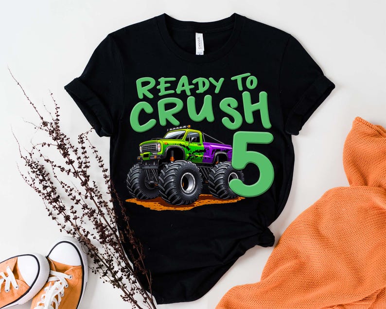 May include: Black t-shirt with a green and purple monster truck graphic and the text "READY TO CRUSH 5". The graphic features a monster truck with large tires. The number 5 is in green.