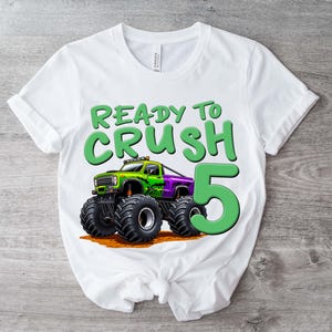 May include: White t-shirt with a graphic of a monster truck and the text "READY TO CRUSH 5". The monster truck is green and purple with large black tires. The number 5 is in green.
