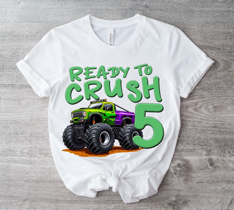 May include: White t-shirt with a graphic of a monster truck and the text "READY TO CRUSH 5". The monster truck is green and purple with large black tires. The number 5 is in green.