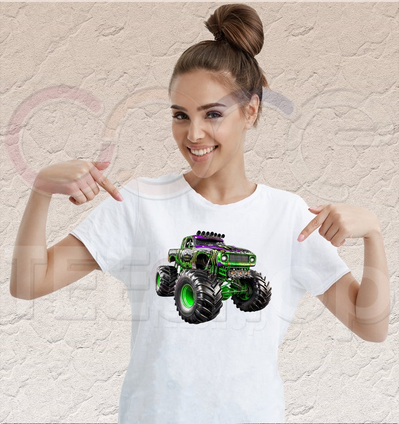 May include: White t-shirt with a green and purple monster truck graphic. The truck has large tires and a black grill.