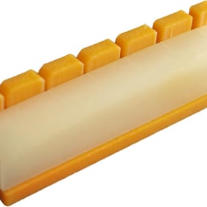 May include: A rectangular, off-white and orange plastic tool with a rounded top and several orange rectangular protrusions. The tool has a smooth, glossy finish and is designed for a specific purpose.