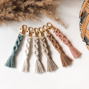 Könnte beinhalten: Sechs bunte Makramee-Schlüsselanhänger mit goldenen Schlüsselringen und Quasten. Die Schlüsselanhänger sind aus verschiedenen farbigen Schnüren gefertigt und haben einen Boho-Stil.
