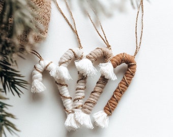 May include: Three handmade candy cane ornaments made of white and brown yarn with gold accents. The ornaments are tied together with a gold string.