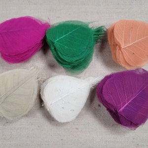 May include: A collection of colorful, dried Bodhi leaves in shades of pink, green, peach, cream, white, and purple. The leaves are arranged in stacks, showcasing their delicate, veined structure. Ideal for crafting and decorative projects.