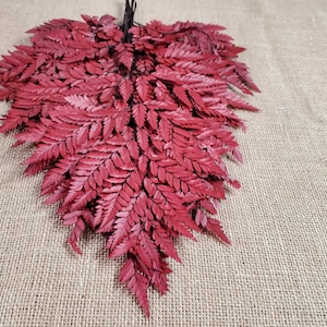 May include: A bunch of red fern leaves arranged in a heart shape on a burlap background.