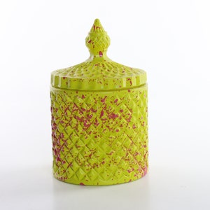 May include: A green glass jar with a diamond pattern and pink splatter paint. The jar has a lid with a pointed top.