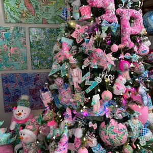 May include: A pink and green Christmas tree decorated with ornaments, bows, and a snowman. The tree is decorated with a pink and green patterned fabric. The tree is decorated with the letters "OP."