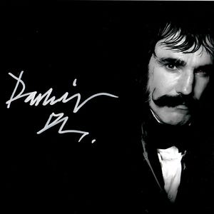 May include: A monochrome photograph of a man with a prominent mustache, dressed in a dark suit and white shirt. The image is signed in white. The man is looking directly at the camera.