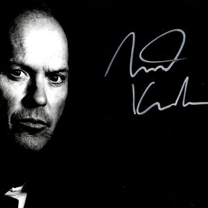 Może przedstawiać: Czarno-białe zdjęcie mężczyzny z poważnym wyrazem twarzy. Obraz to portret z podpisem w prawym górnym rogu na czarnym tle.