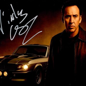 May include: An autographed photo featuring a man in a leather jacket, standing in front of a classic car. The car is a dark color with black racing stripes. The signature is in white ink.