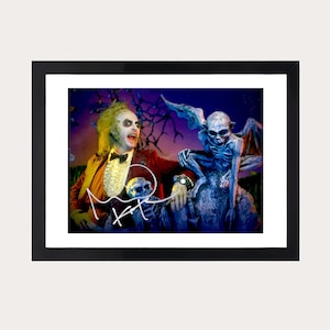 Może przedstawiać: Oprawiony wydruk przedstawiający postać z dzikimi blond włosami, ubraną w czerwony garnitur i muszkę, ze szkieletem i niebieskim gargulcem. Wydruk jest podpisany na biało. Rama jest czarna.