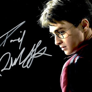 Puede incluir: Fotografía firmada de un joven con gafas y una camisa roja y negra, sobre un fondo negro. La firma, en tinta blanca, es prominente. Es un retrato de un actor famoso.