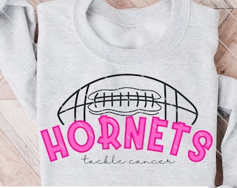Puede incluir: Sudadera gris claro con un diseño de balón de fútbol y la palabra "Hornets" en rosa brillante. Debajo de la palabra "Hornets" está la frase "tackle cancer". La sudadera también presenta el texto "J Rae Design Co."