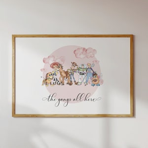 Op de afbeelding: Een ingelijste aquarelprint met personages uit een populaire animatiefilm, waaronder een hond, een cowgirl, een paard, een ruimtevaarder, een cowboy en een aardappel. De personages staan tegen een roze cirkel met wolken, met de tekst "the gang's all here" eronder.