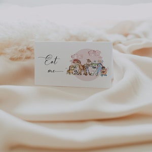 K&ouml;nnte beinhalten: Eine wei&szlig;e Karte mit den Worten "Eat me" in eleganter Schrift. Die Karte zeigt eine Aquarellillustration von Zeichentrickfiguren, darunter ein Hund, ein Pferd und ein Weltraumranger, vor einem rosa Hintergrund.