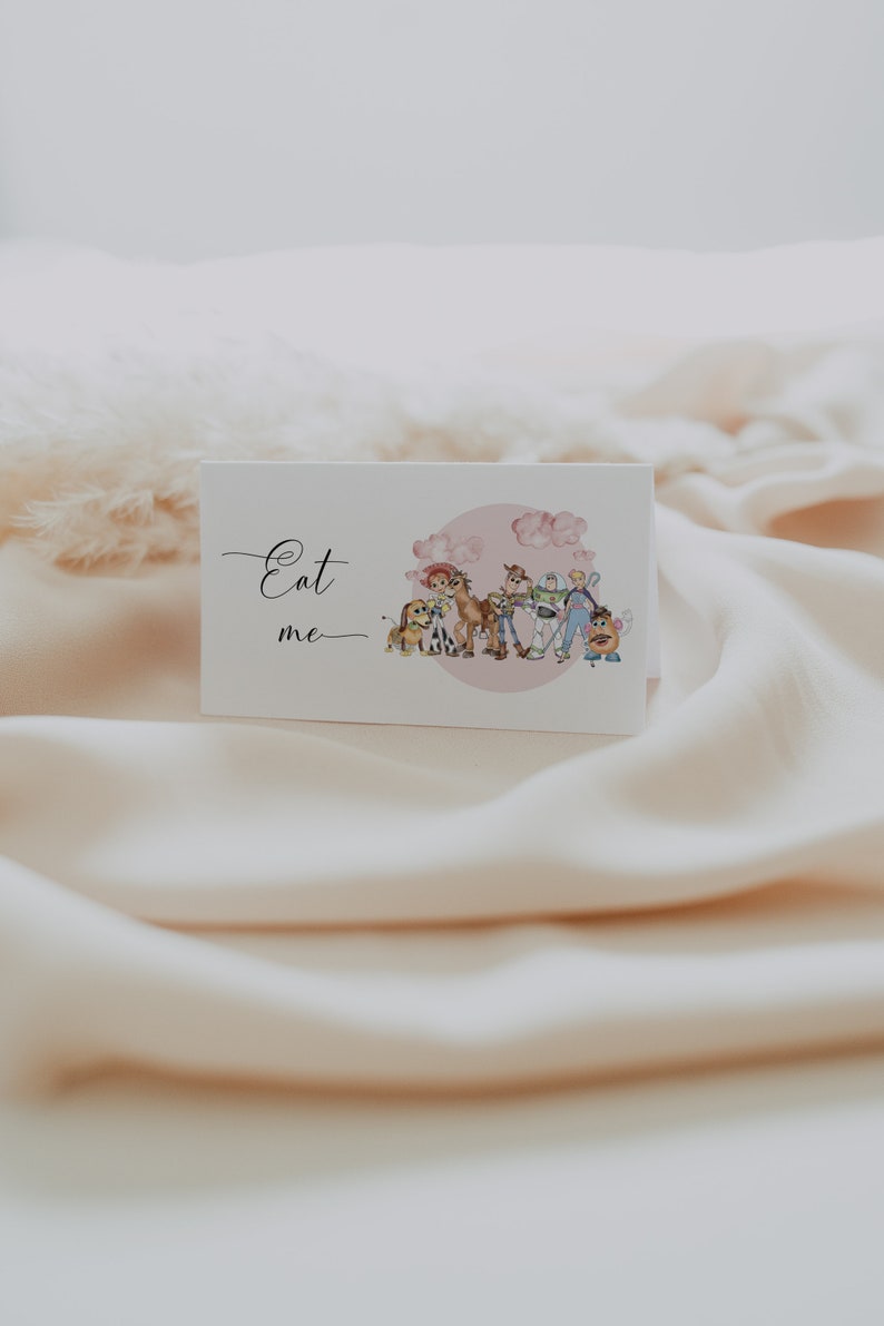 K&ouml;nnte beinhalten: Eine wei&szlig;e Karte mit den Worten "Eat me" in eleganter Schrift. Die Karte zeigt eine Aquarellillustration von Zeichentrickfiguren, darunter ein Hund, ein Pferd und ein Weltraumranger, vor einem rosa Hintergrund.