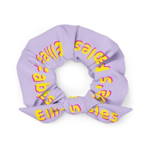 May include: A purple scrunchie with a yellow and pink design that says "It's a vibe" in a retro font.