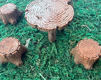 May include: A brown miniature table and three matching stools, each designed to resemble a tree stump with visible circular wood grain patterns on the top surfaces and textured bark details on the sides, arranged in a small grouping.