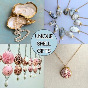 May include: A collection of jewelry featuring oyster and scallop shells with gold-painted edges, paired with white pearls on metal chains. The image includes a central circular graphic with the text UNIQUE SHELL GIFTS in black lettering.