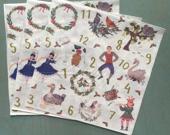 Puede incluir: Una pila de servilletas de papel blancas con ilustraciones y números. Cada servilleta presenta una imagen diferente, incluyendo bailarines, pájaros y una vaca. Se muestran los números del 1 al 12, junto con coronas decorativas y detalles florales.