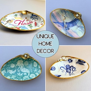 Puede incluir: Cuatro conchas decorativas con bordes pintados en oro. Una muestra un mapa de Florida con un ave y delfines, otra una garza azul, una tiene un patr&oacute;n de sirena turquesa y la &uacute;ltima un pulpo azul y vida marina. Cada concha tiene una perla.