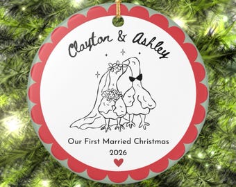 May include: A round ceramic Christmas ornament with a scalloped red border. The white center features a black line drawing of two geese, one wearing a veil and flowers, the other a bowtie. Text reads: Clayton & Ashley, Our First Married Christmas 2026.