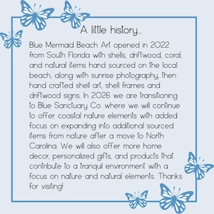 Puede incluir: Un letrero cuadrado de color azul claro con un borde azul oscuro e ilustraciones de mariposas en las esquinas. El texto dice: A little history... Blue Mermaid Beach Art opened in 2022 from South Florida with shells, driftwood, coral, and natural items.