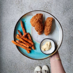 K&ouml;nnte beinhalten: Ein blauer und wei&szlig;er Keramikteller mit zwei paniertem H&uuml;hnchen-Tenders, S&uuml;&szlig;kartoffel-Pommes und einer kleinen Sch&uuml;ssel Dipsauce.