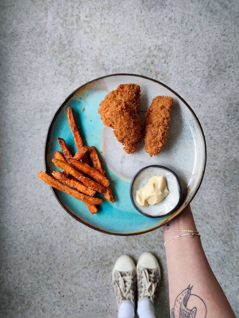 K&ouml;nnte beinhalten: Ein blauer und wei&szlig;er Keramikteller mit zwei paniertem H&uuml;hnchen-Tenders, S&uuml;&szlig;kartoffel-Pommes und einer kleinen Sch&uuml;ssel Dipsauce.