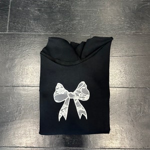 May include: Black sweatshirt with a white lace bow design.