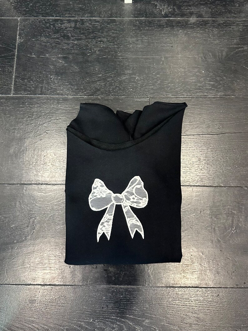 May include: Black sweatshirt with a white lace bow design.