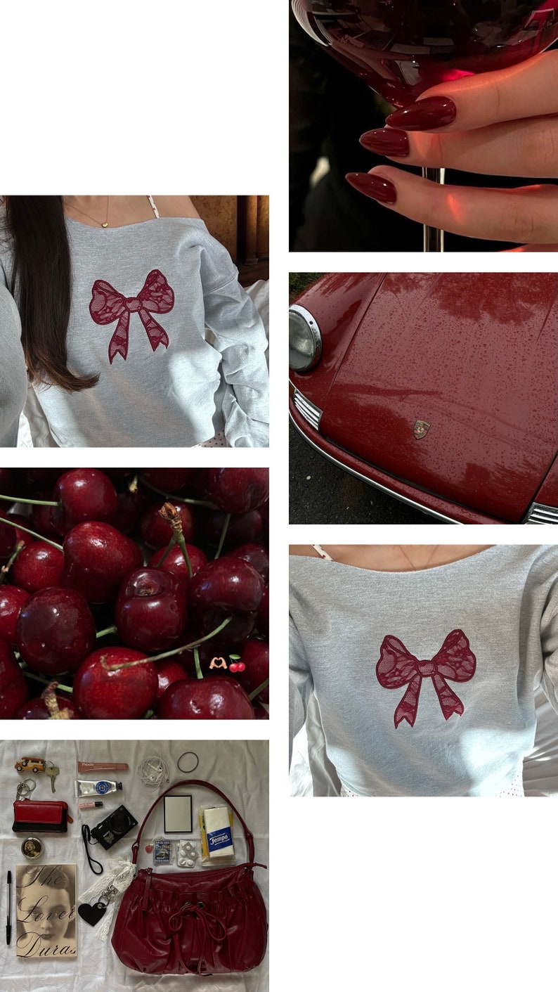 May include: A gray off-the-shoulder sweatshirt with a burgundy lace bow on the front. The sweatshirt is worn by a person with long dark hair. The background is a blurry image of a room.