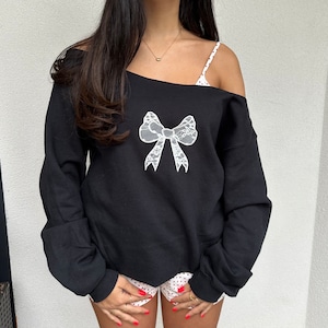 May include: Black off-the-shoulder sweatshirt with a white lace bow design.