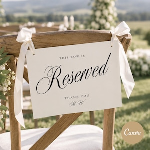 May include: A rectangular white sign attached to a wooden chair with cream-colored ribbons. The sign features black text that reads THIS ROW IS Reserved, followed by THANK YOU and the initials M.W in a decorative script font style.