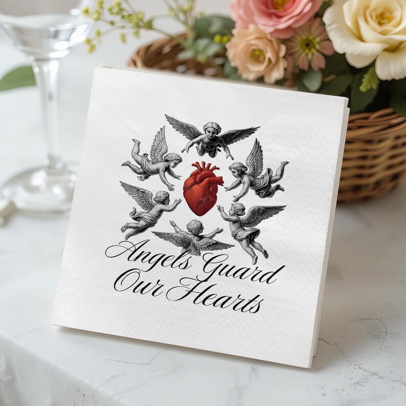 May include: White square paper napkin with a design featuring cherubs surrounding a red heart. The text "Angels Guard Our Hearts" is written in elegant script below the cherubs. The napkin is on a white surface.