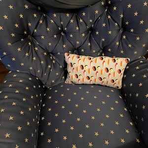 May include: A navy blue armchair with a gold star pattern. A small rectangular pillow with a sushi pattern rests on the chair. A black blanket is draped over the back of the chair.