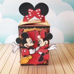 Peut inclure: Une bo&icirc;te en carton rouge et jaune avec une image 3D de Mickey Mouse et Minnie Mouse. Mickey Mouse porte un short rouge et des chaussures jaunes. Minnie Mouse porte une robe rouge &agrave; pois blancs et des chaussures rouges. La bo&icirc;te a un n&oelig;ud rouge &agrave; pois blancs sur le dessus.