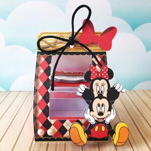 Peut inclure: Une bo&icirc;te &agrave; carreaux rouges et noirs avec une fen&ecirc;tre transparente, repr&eacute;sentant Mickey Mouse et Minnie Mouse. La bo&icirc;te est orn&eacute;e d'un ruban noir avec un n&oelig;ud rouge et de perles.