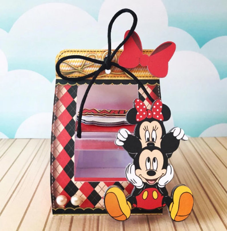 Peut inclure: Une bo&icirc;te &agrave; carreaux rouges et noirs avec une fen&ecirc;tre transparente, repr&eacute;sentant Mickey Mouse et Minnie Mouse. La bo&icirc;te est orn&eacute;e d'un ruban noir avec un n&oelig;ud rouge et de perles.