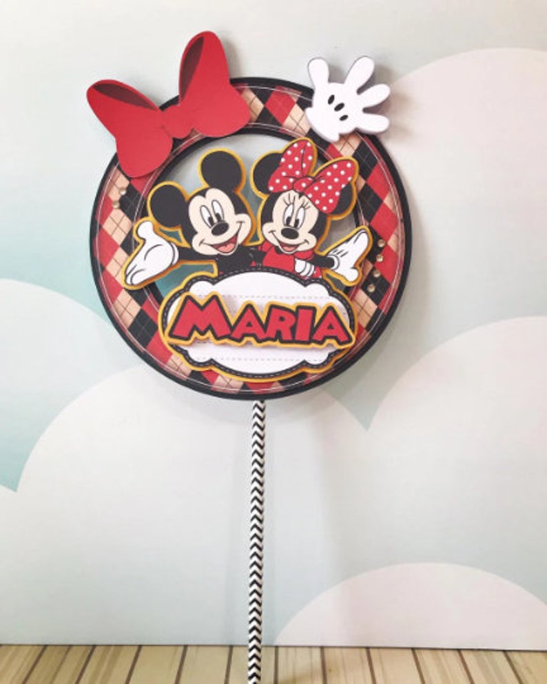 Peut inclure: Un topper de g&acirc;teau rouge, noir et blanc repr&eacute;sentant Mickey et Minnie Mouse. Le topper a un n&oelig;ud rouge, un gant blanc et un nuage jaune avec le nom "MARIA" &eacute;crit dessus.