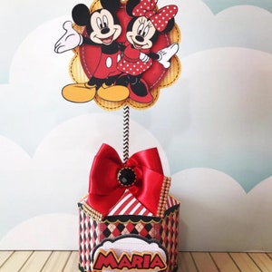 Peut inclure: Bo&icirc;te hexagonale rouge et noire avec un dessus ray&eacute; rouge et blanc et un n&oelig;ud rouge. La bo&icirc;te a une &eacute;tiquette blanche avec le nom "MARIA" en lettres dor&eacute;es. Un topper Mickey Mouse et Minnie Mouse est plac&eacute; sur le dessus de la bo&icirc;te.