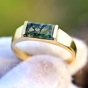 May include: A gold ring with a green moss agate gemstone. The gemstone is rectangular in shape and has a unique pattern.