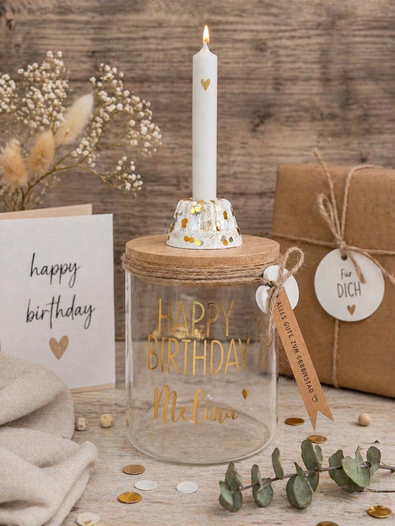 Op de afbeelding: Een glazen pot met houten deksel en gouden tekst "HAPPY BIRTHDAY Melina". Een witte kaars met een gouden hart in een decoratieve houder. Een verjaardagskaart en een cadeau zijn ook aanwezig, wat een feestelijke sfeer cre&euml;ert.