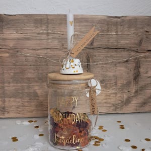 Op de afbeelding: Een glazen pot gevuld met gummy snoepjes, een houten deksel en een witte kaars met een gouden hart. De pot is versierd met gouden letters met de tekst "Happy Birthday Jacqueline". Een klein label leest "Voor jou".