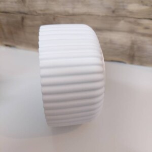 Puede incluir: Maceta de cer&aacute;mica blanca con dise&ntilde;o acanalado.