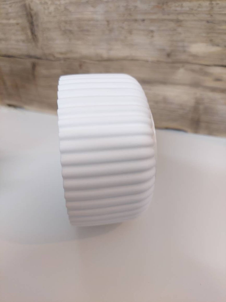 Puede incluir: Maceta de cer&aacute;mica blanca con dise&ntilde;o acanalado.