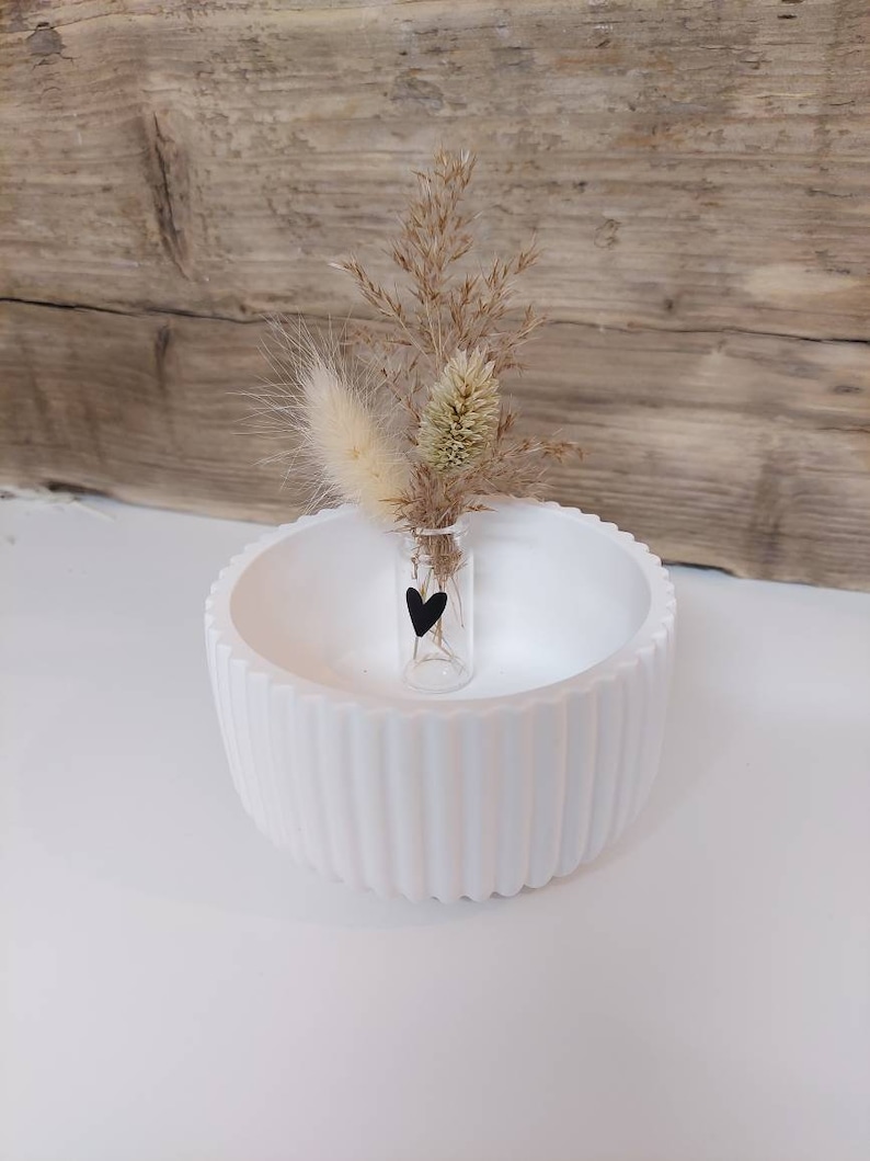 Puede incluir: Un cuenco de cer&aacute;mica blanco con un peque&ntilde;o jarr&oacute;n de vidrio que contiene hierbas secas y una pegatina de coraz&oacute;n negro. El jarr&oacute;n est&aacute; en el centro del cuenco.