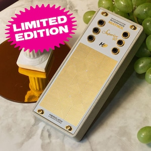 Puede incluir: Un módulo Man-Machine Interface Matrix Superior 98 de edición limitada, blanco y dorado, de Herzlich Laboratories. El módulo tiene un patrón de cuadrícula y múltiples conectores dorados.