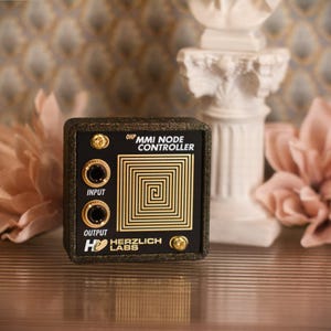 May include: A black and gold MMI Node Controller with the text "OHP MMI NODE CONTROLLER" and "INPUT" and "OUTPUT". The controller has a gold spiral design and two gold screws. The brand name "HERZLICH LABS" is also visible.